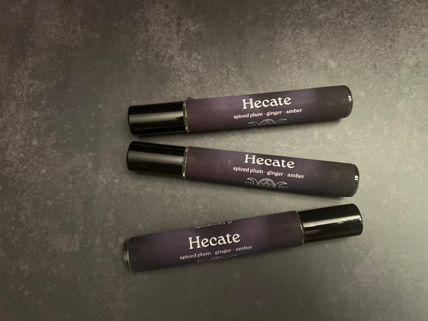 Three Hecate perfumes on a gray surface