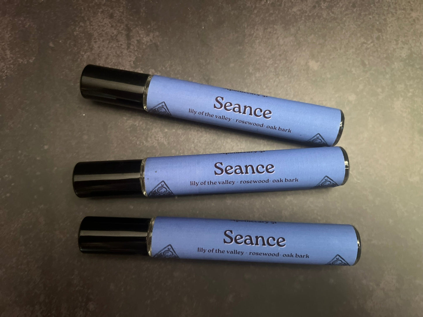 Three Seance perfumes with blue bodies and black caps on a gray surface