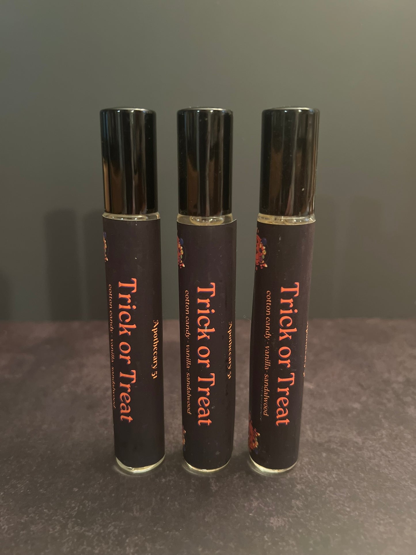 Three 'Trick or Treat' perfume bottles on a gray background